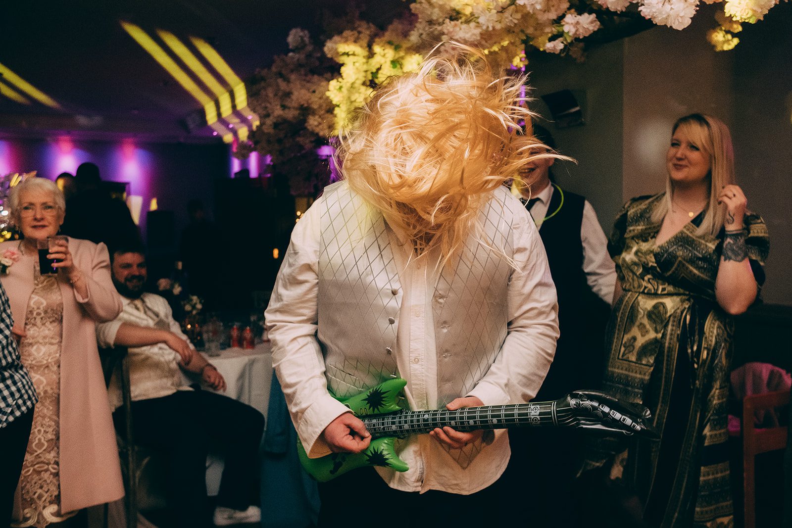 Wedding Guest in a blonde wig, headbanging with a blow up guitar